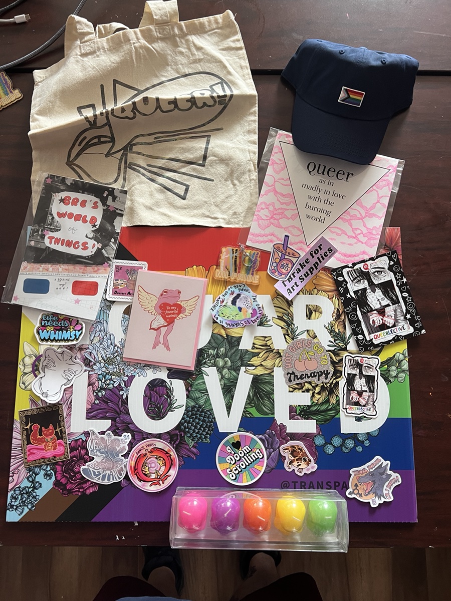 Raffle Basket 2 with a Queerlective tote, cap, cards, art, stickers, and colorful gifts